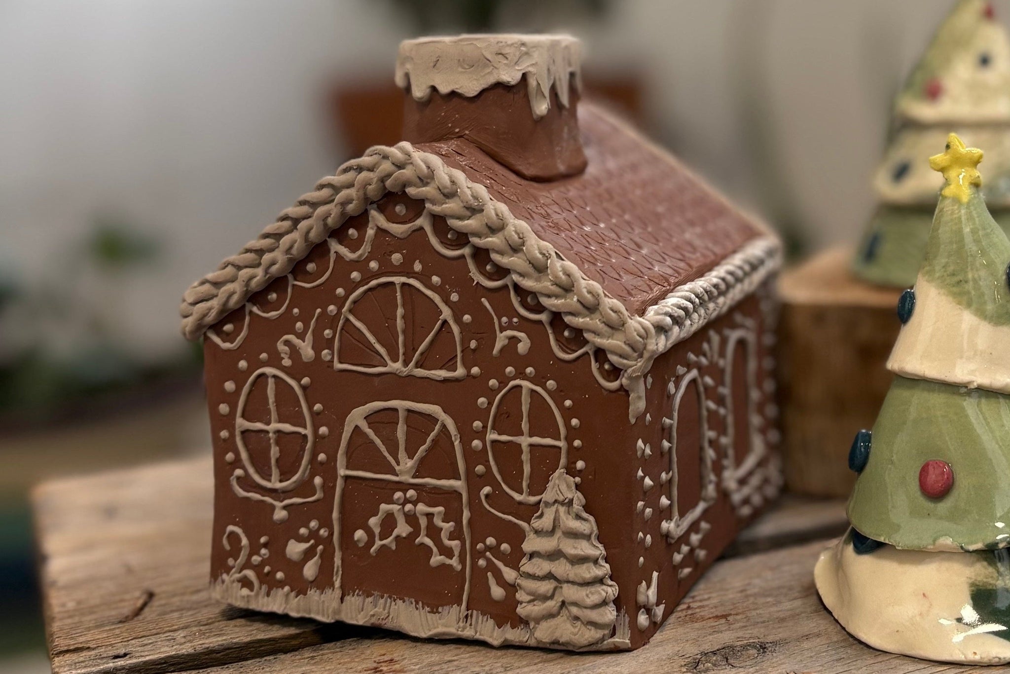 Decorative gingerbread house and tree on a wooden surface with a blurred indoor background