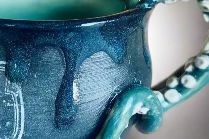 Teal ceramic mug with a unique handle design on a neutral background