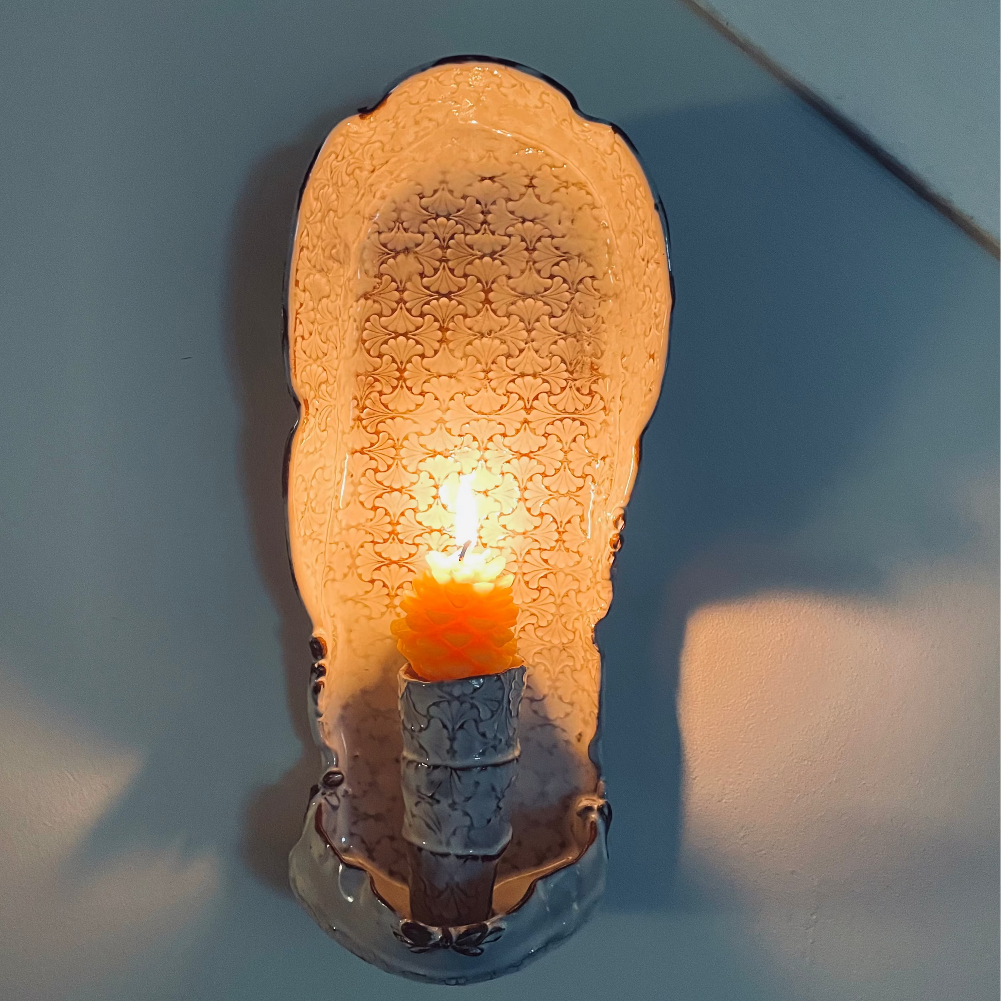 Patterned ceramic wall sconce made with red stoneware holding lit beeswax candle