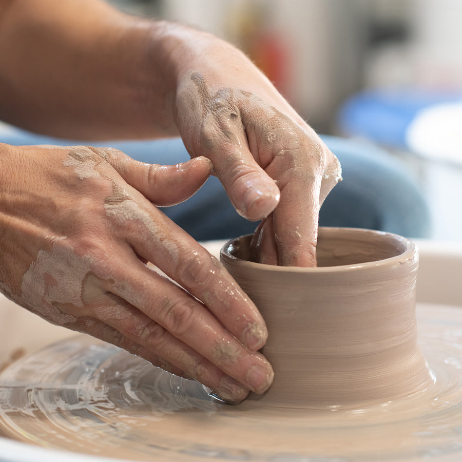 A person's hands using a pottery wheel to shape a clay bowl.